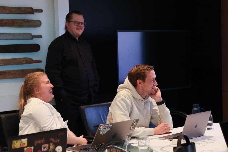 Tre kolleger i Link Utvikling som ler rundt et møtebord med laptoper