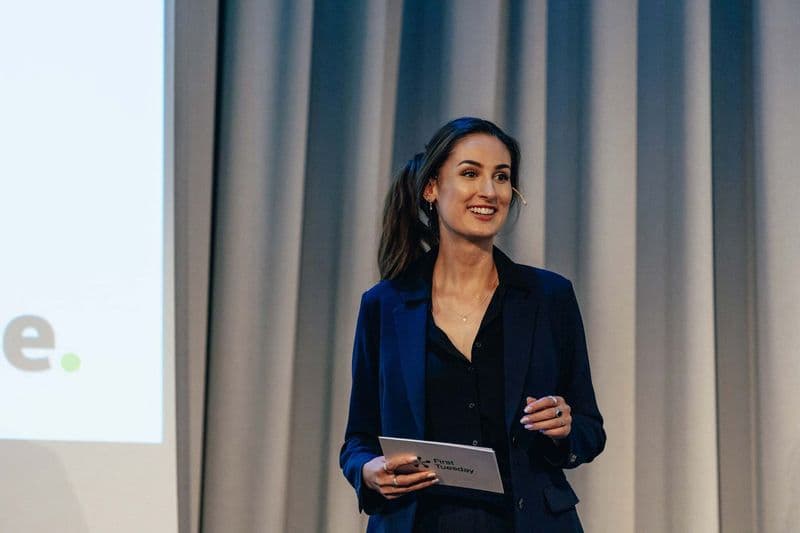 Hana Colakovic smiler på scenen med First Tuesday-kort i hendene